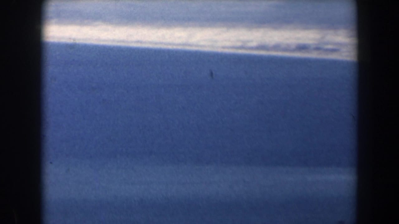 1960 Israel 8mm frame of open sea and a pale coastline or surf band, seen through dark gate edges.
