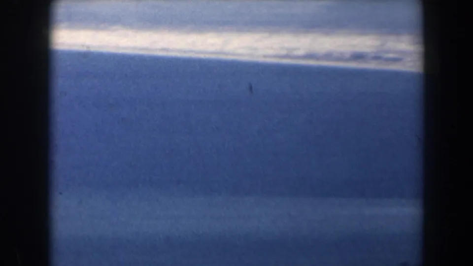 1960 Israel 8mm frame of open sea and a pale coastline or surf band, seen through dark gate edges.