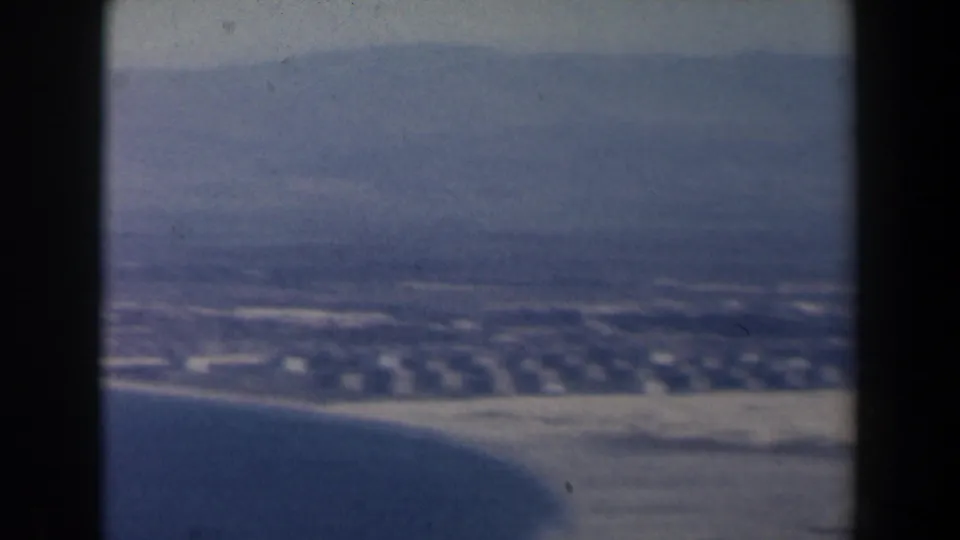 1960 Israel 8mm frame showing a coastal settlement, blue water, and hazy mountains from an elevated viewpoint.