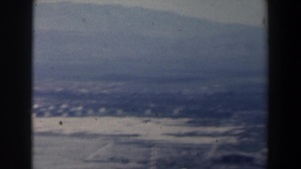 1960 Israel home-movie aerial view of pale shoreline, water and hazy mountains seen through dark aircraft window framing.
