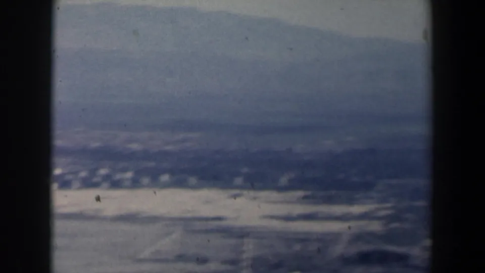 1960 Israel home-movie aerial view of pale shoreline, water and hazy mountains seen through dark aircraft window framing.