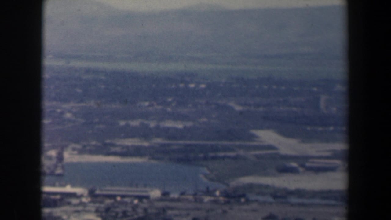 Aerial view of water, shoreline, low buildings and distant hills.