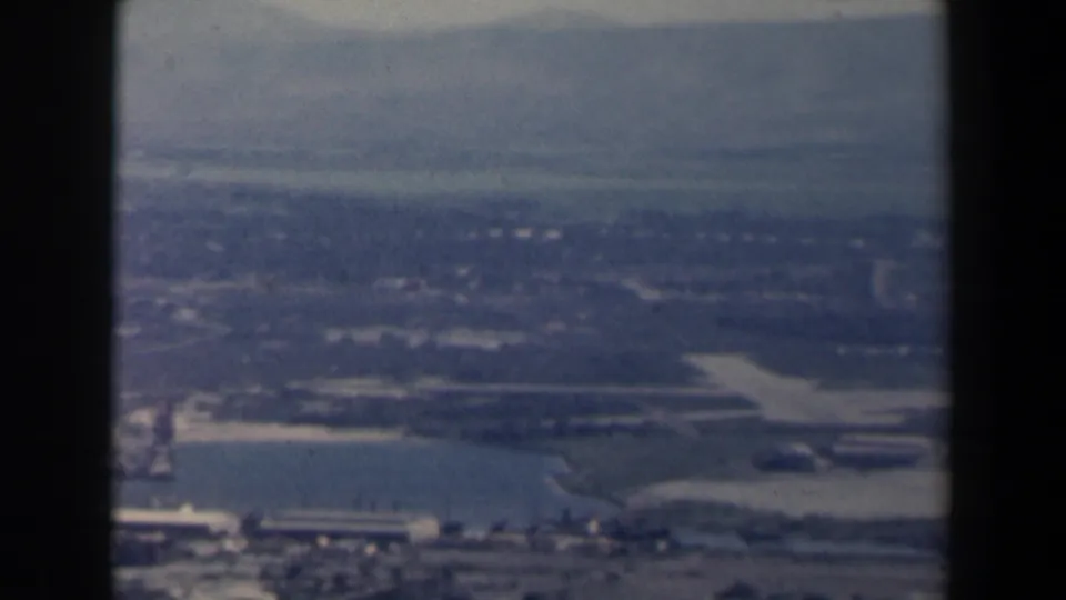 1960 Israel aerial frame showing a water body, shoreline, low buildings and hazy hills beyond the aircraft window.