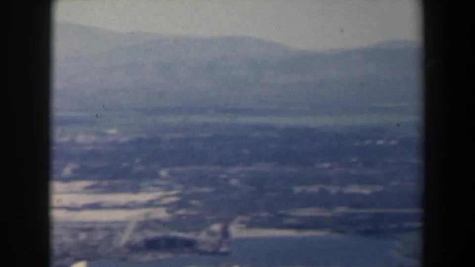 1960 Israel home-movie aerial frame with hazy mountains, open terrain, shoreline and water seen from an aircraft.