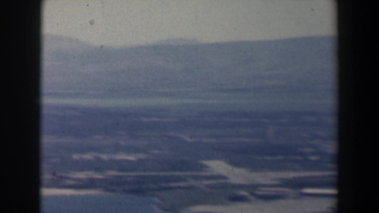 Hazy aerial view of fields and distant mountains through dark window edges.