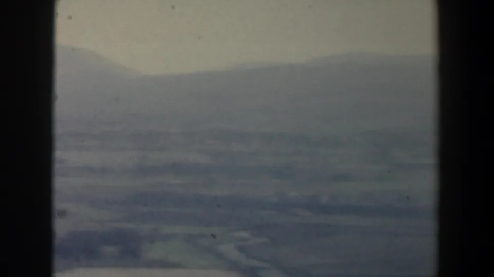 Blue-green 8mm frame of hazy open terrain in Israel, with low hills, fields, and window framing at the edge.