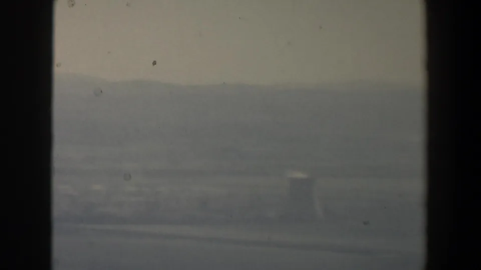 Hazy 1960 Israel aerial frame with distant hills, muted fields, and a faint rectangular structure visible near the lower right.