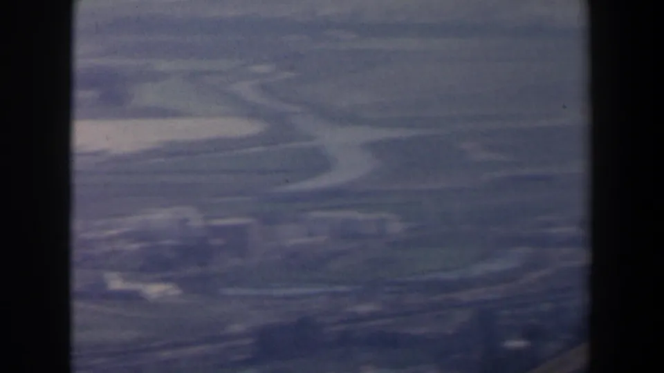 Distant 1960 Israel valley landscape with winding roads, soft haze, and faint buildings on a hillside at the upper right.