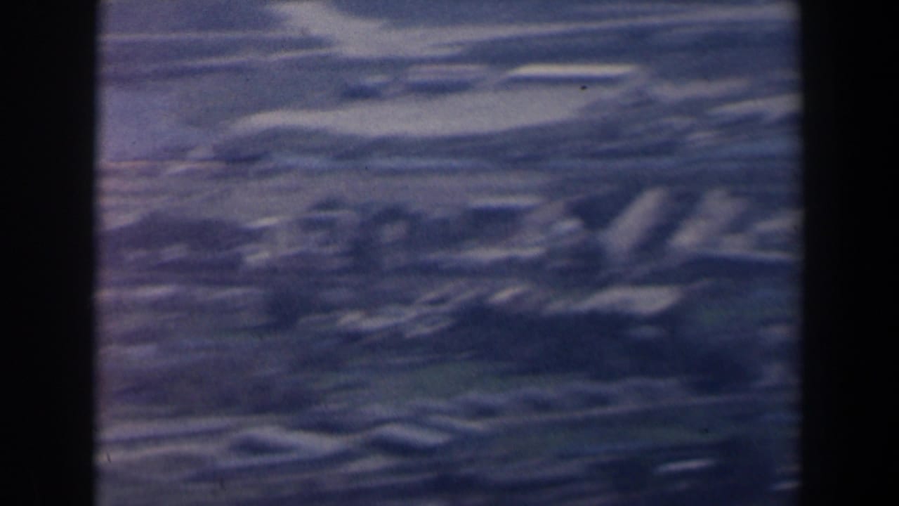 Blue-tinted 1960 Israel aerial frame with fields, winding roads, and indistinct low buildings across rural terrain.