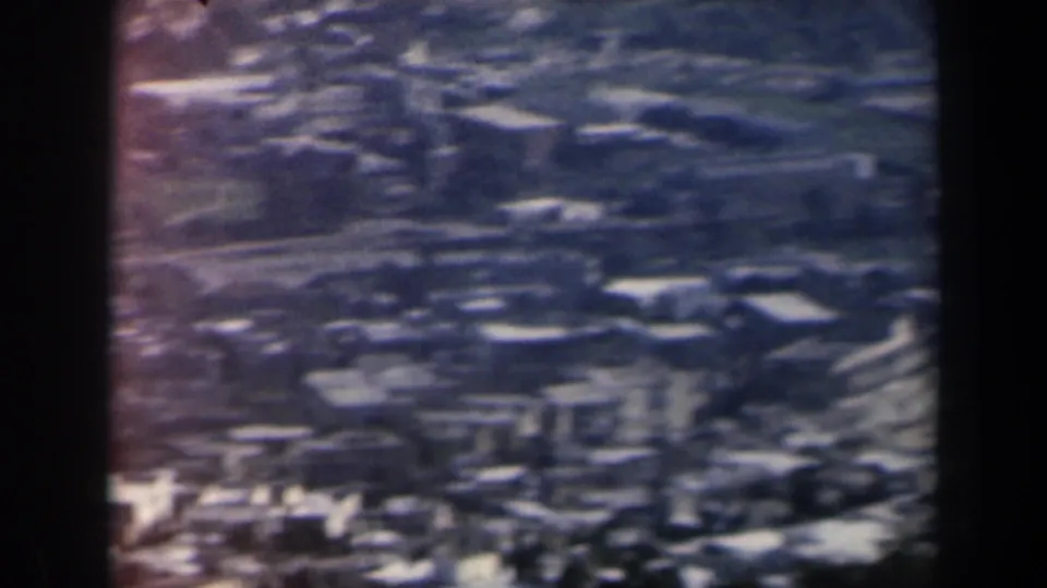 1960 Israel aerial home-movie frame showing clustered structures, roads, open fields, and darker planted areas.