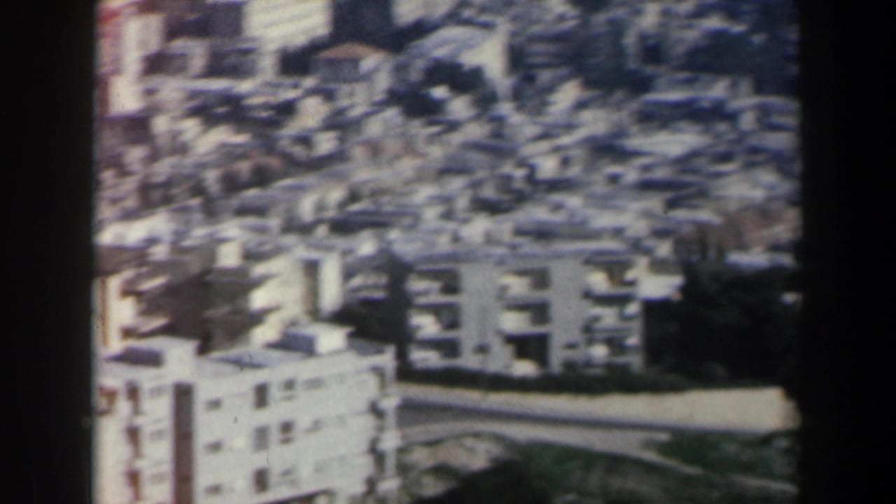 1960 Israel 8mm aerial view of grey apartment buildings and dense urban blocks seen through soft, grainy film.