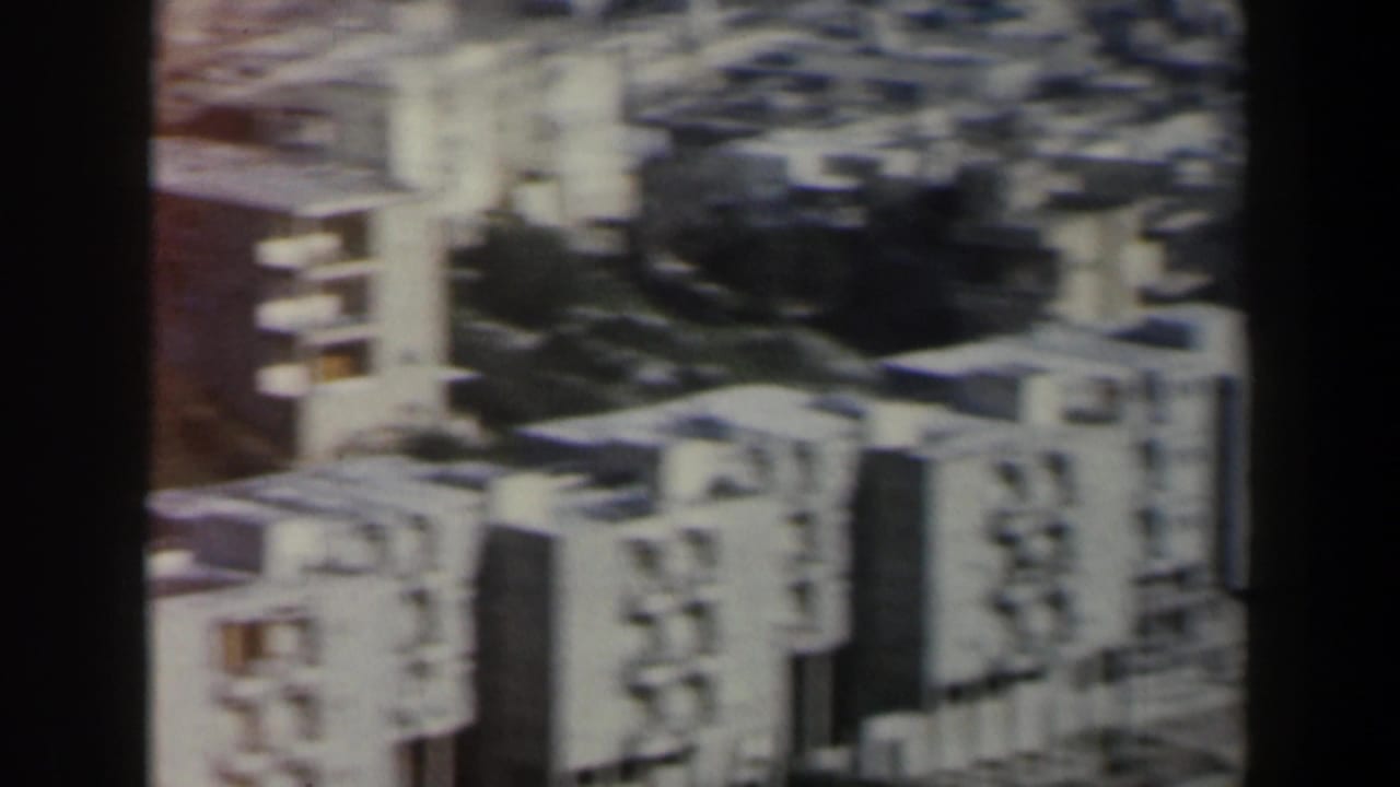 Aerial home-movie view in Israel showing block-style residential buildings, shadowed open ground, and soft 8mm color fading.