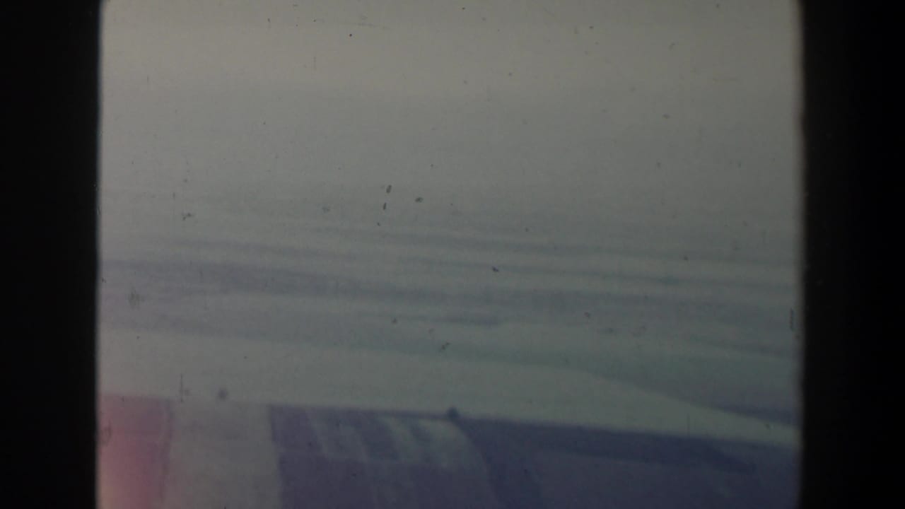 1960 Israel home-movie frame showing a hazy aerial landscape through an airplane window, with pale sky and soft hills below.