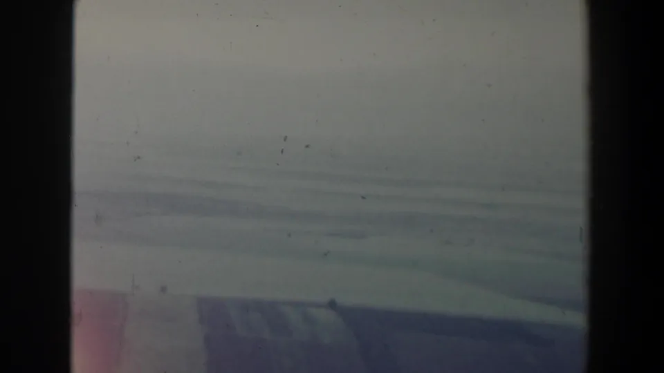 1960 Israel home-movie frame showing a hazy aerial landscape through an airplane window, with pale sky and soft hills below.
