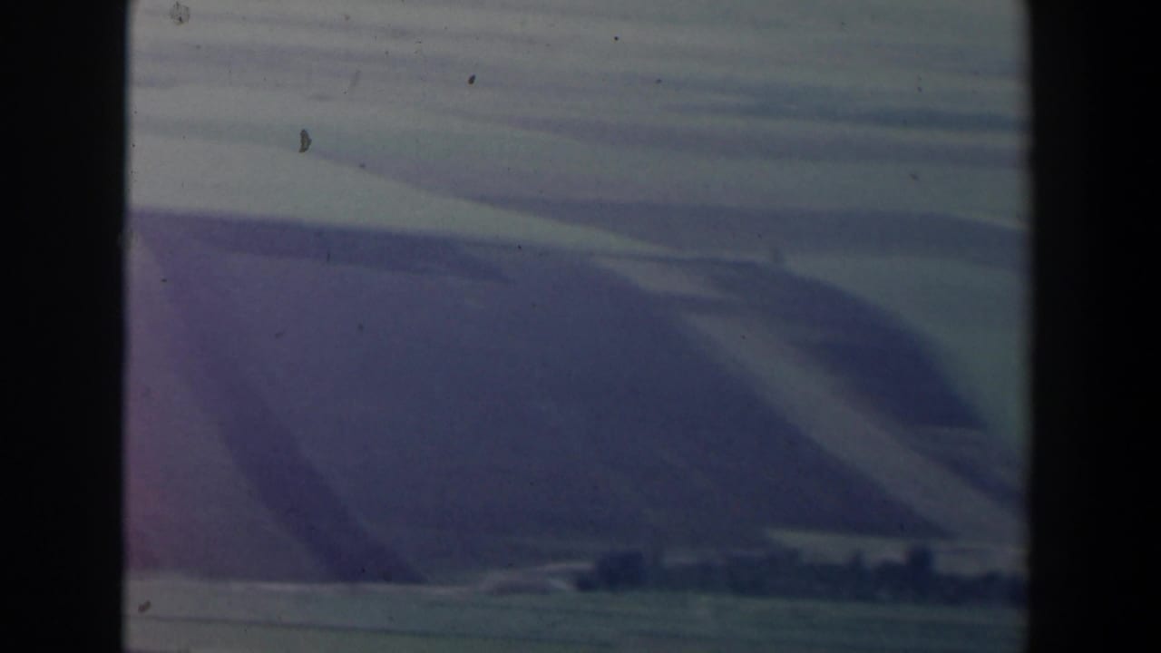 Aerial view over Israel from an airplane window, with muted hills, haze, and dark frame edges from the cabin view.