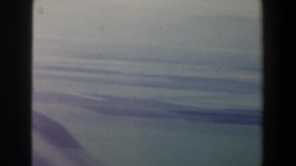 1960 home-movie still of hazy fields and low hills seen from an airplane window over Israel, with grain and faded color.