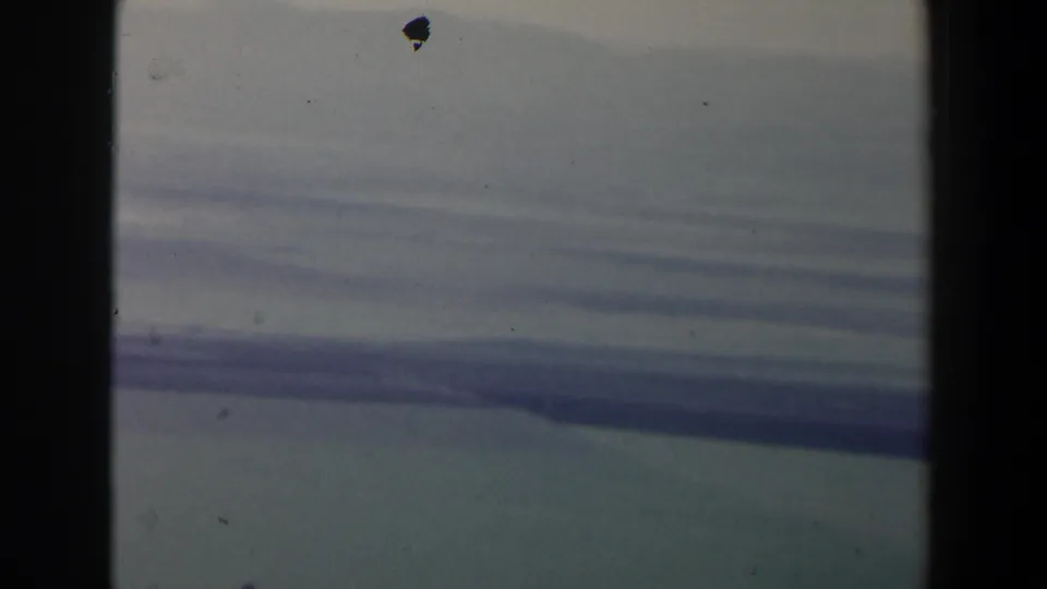 A steady airplane-window view over hazy Israeli terrain, with a pale horizon, dark cabin framing, and visible dust on the 8mm scan.