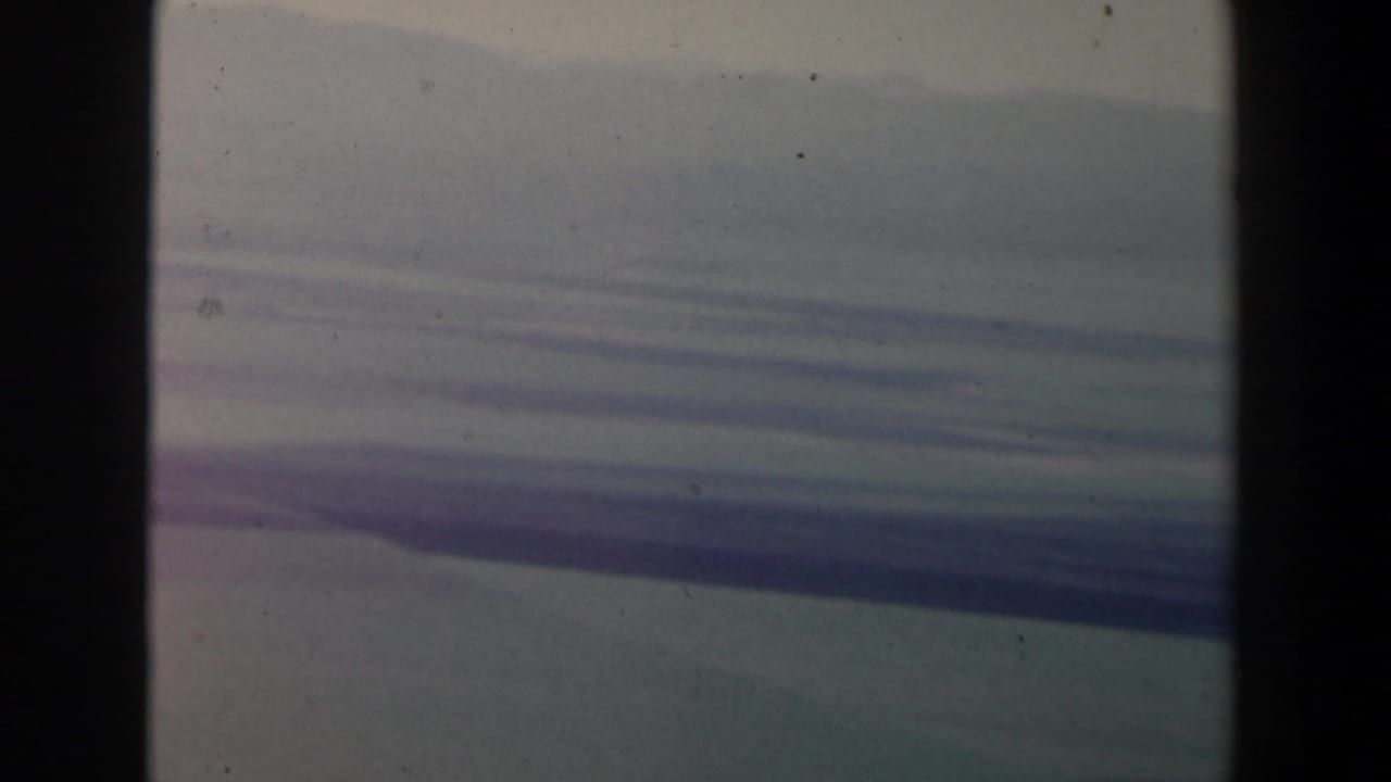 Layered blue-gray cloud bands over a hazy landscape, seen through a dark film frame edge.