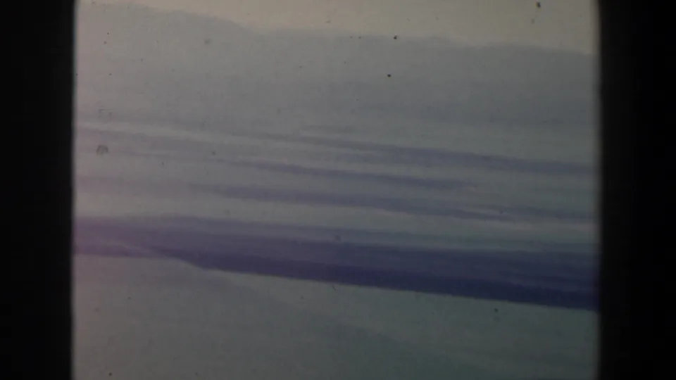 1960 Israel 8mm frame showing hazy blue-gray cloud layers above a subdued landscape with visible film grain and gate edges.