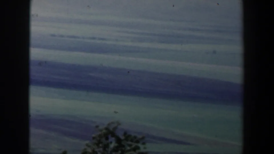 1960 Israel 8mm frame showing blue-gray cloud bands above a dark foreground silhouette that may be trees or hillside.