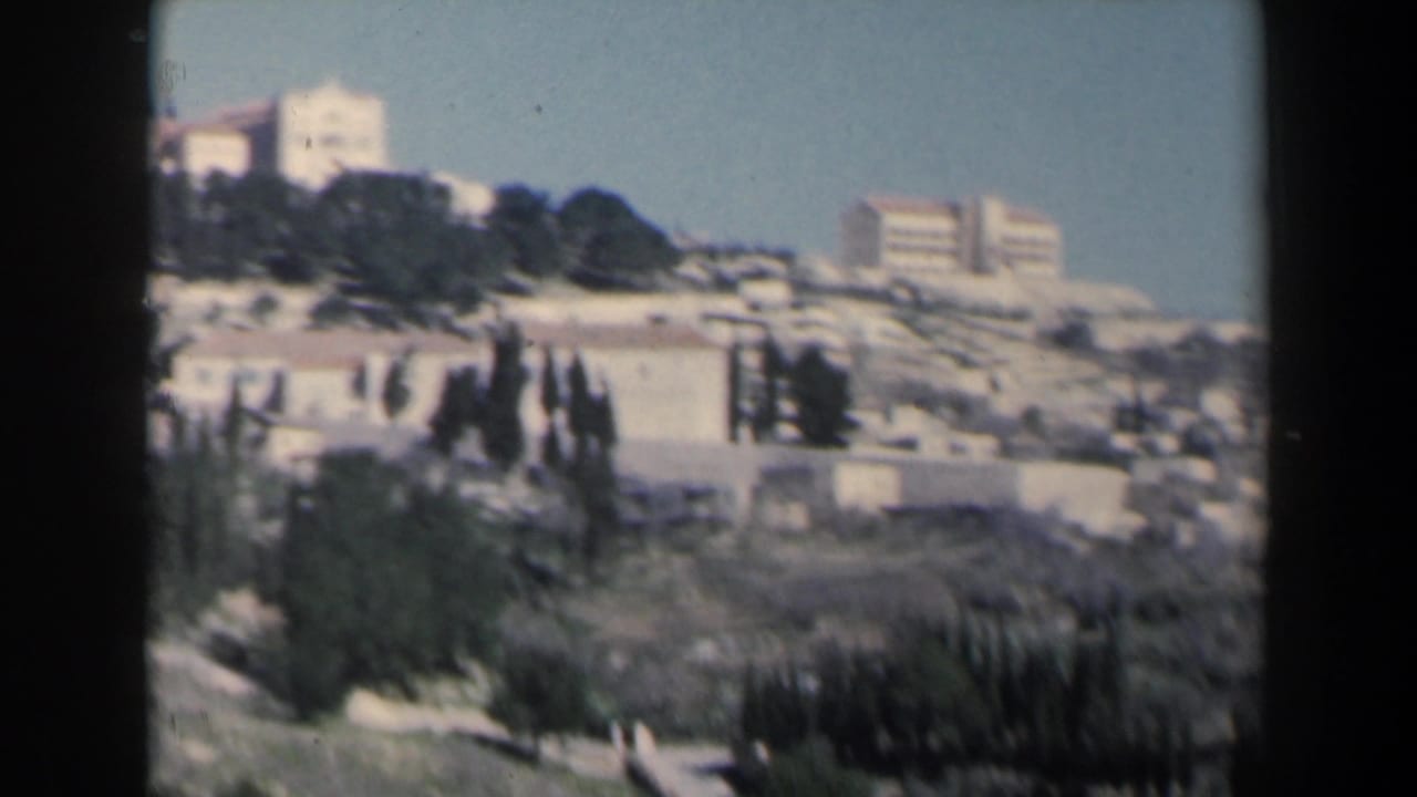 1960 Israel home-movie view of pale hillside buildings, terraces, and cypress-like trees under a clear sky.