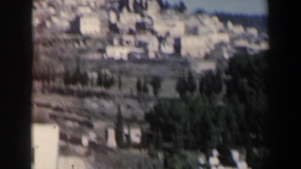 Soft 8mm view of an Israeli hillside area with pale structures, terraces, and dense dark vegetation.