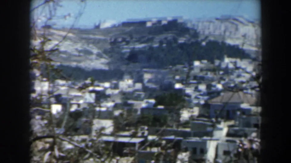 Wide 1960 Israel view of clustered white houses below rocky hills, framed by branches and film borders.