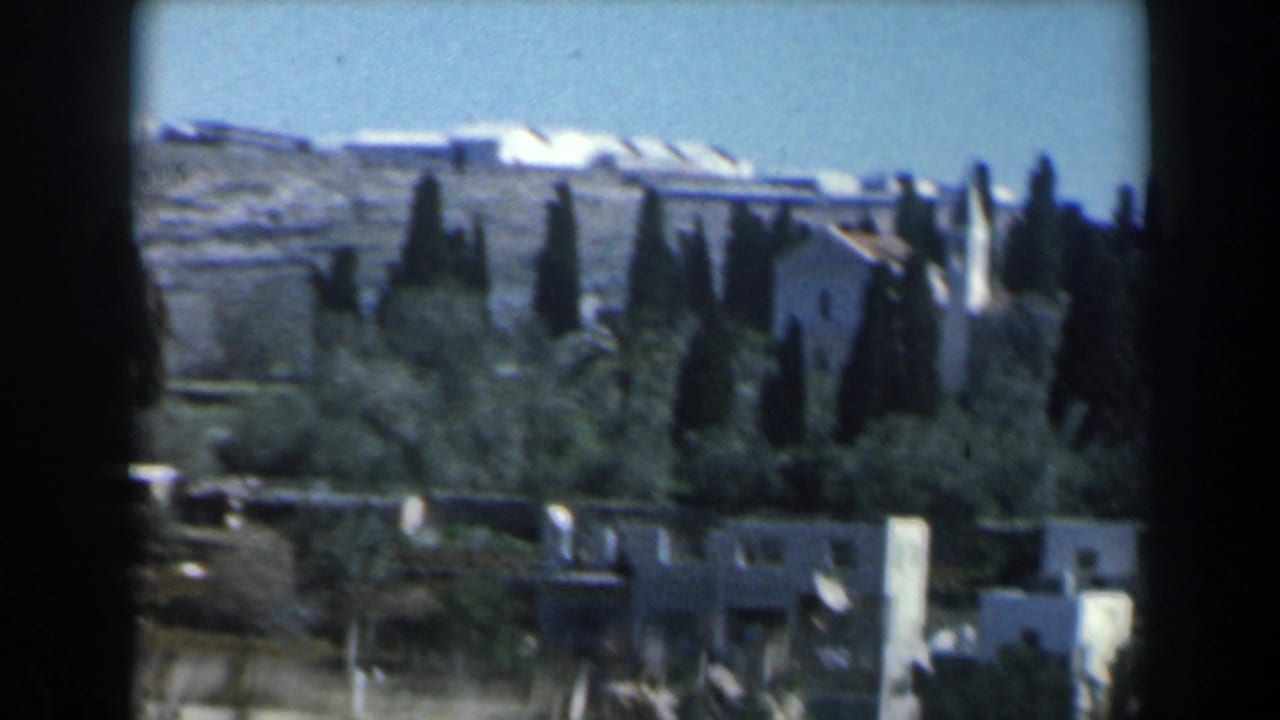 Distant hillside houses and dark trees under a blue sky.