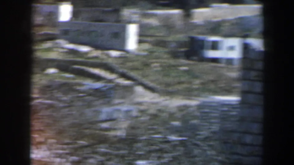 1960 Israel 8mm frame showing rocky terrain, low walls, and small pale hillside buildings.