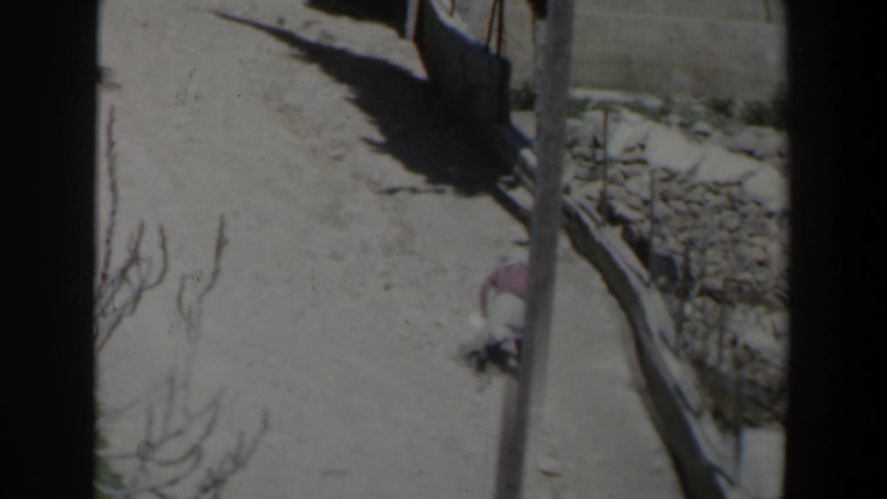 Elevated view of a narrow path beside stone walls with a small veiled figure partly visible.