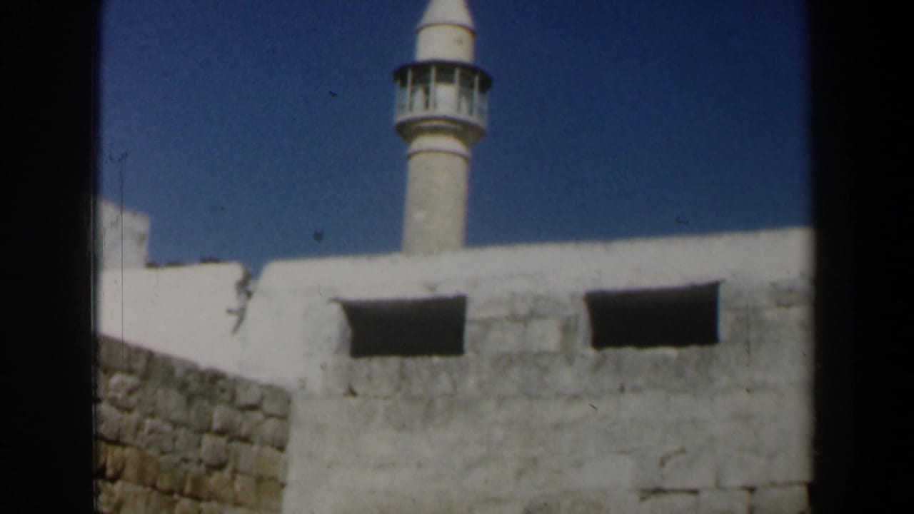 White mosque minaret rising behind white stone walls under a blue sky.