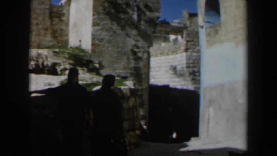 1960 Israel frame showing distant silhouetted pedestrians in a stone alley near whitewashed buildings.