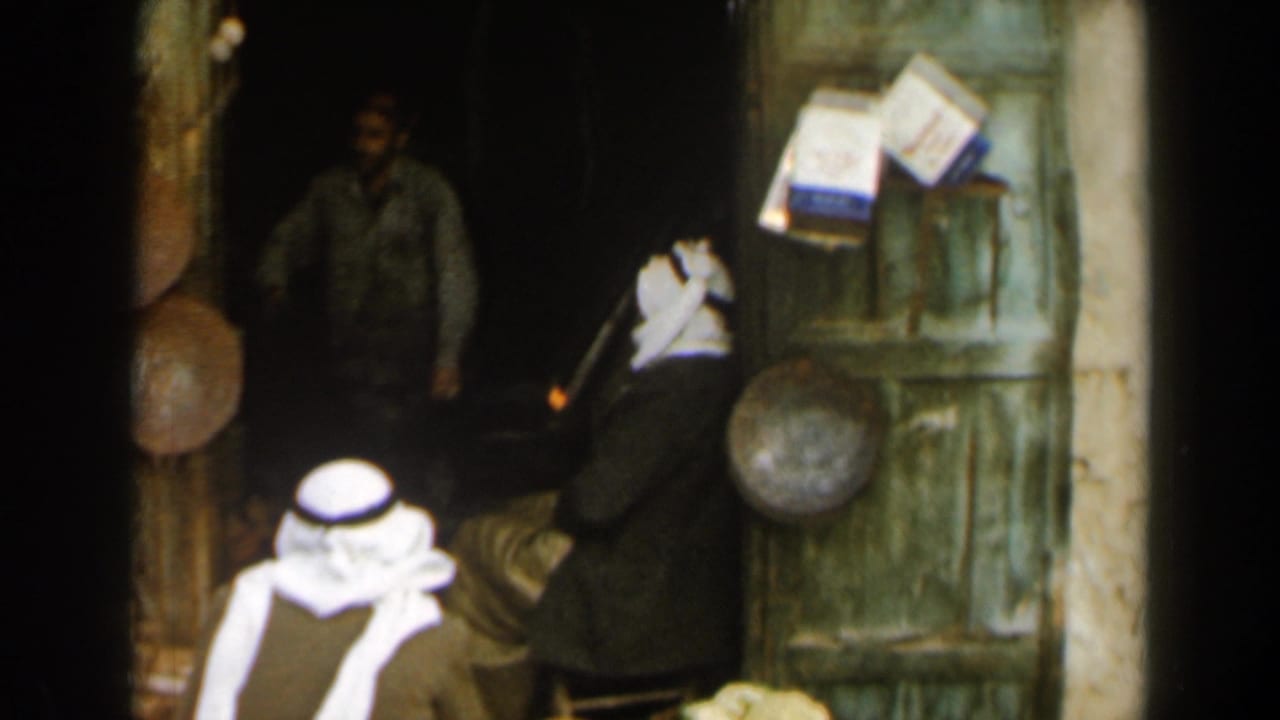 A man in a grey shirt stands in a dark shop doorway as robed men face the entrance.