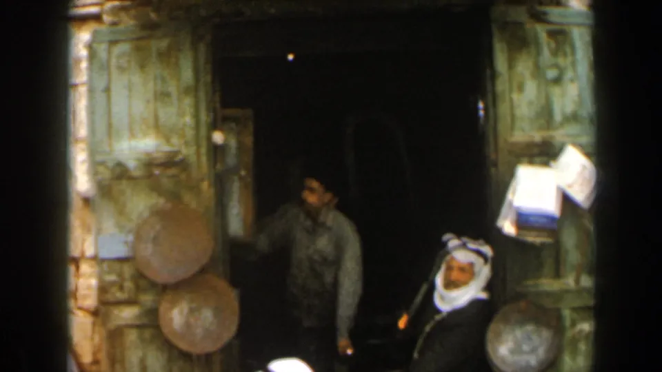 1960 Israel home-movie view of a rustic shop front with green woodwork, metal pans, and men gathered near the doorway.