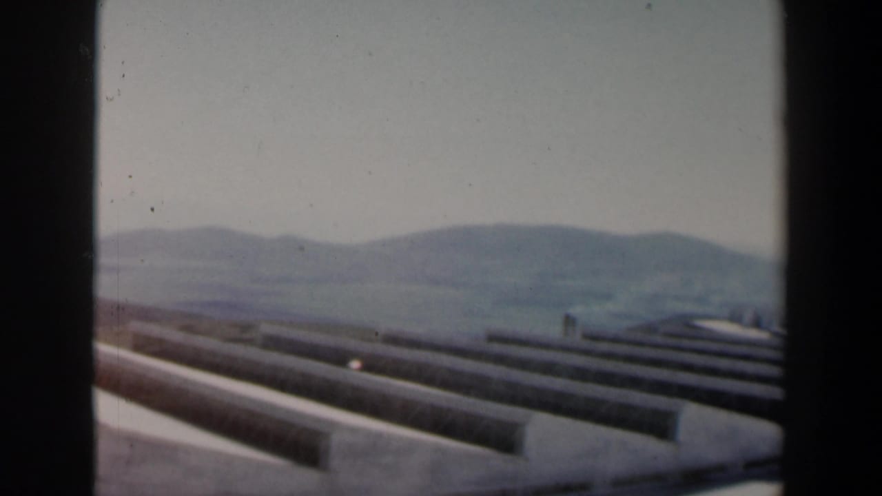 Long concrete roof or stair elements recede toward hills in the distance.
