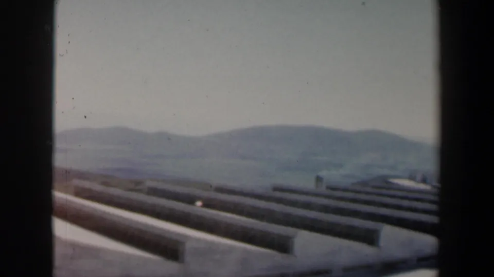 A visitor-shot 8mm view in Israel shows repeated concrete lines running across a hillside, with hazy hills behind them.