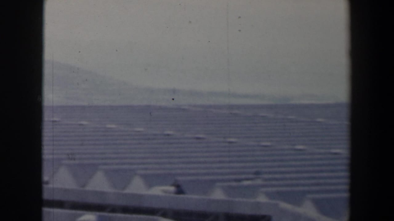 1960 Israel view across a broad roofed complex with angular white roof forms and a hazy hillside in the distance.