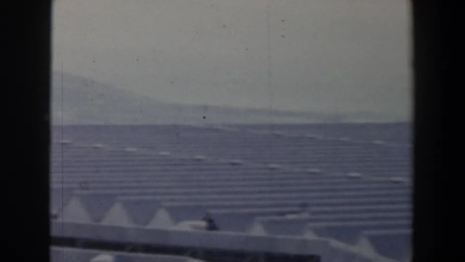 1960 Israel view across a broad roofed complex with angular white roof forms and a hazy hillside in the distance.