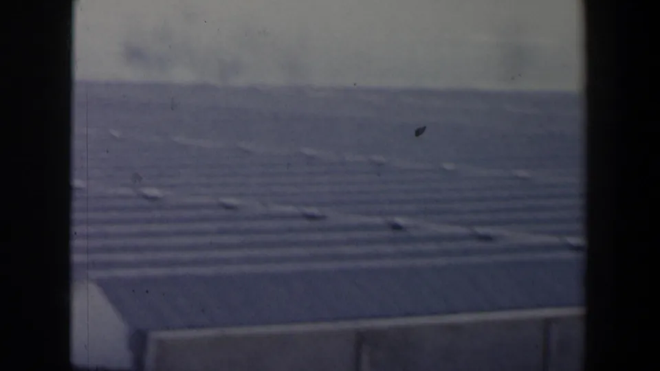1960 Israel 8mm frame with a hazy high-angle view over a large roof, concrete wall, and distant landscape.
