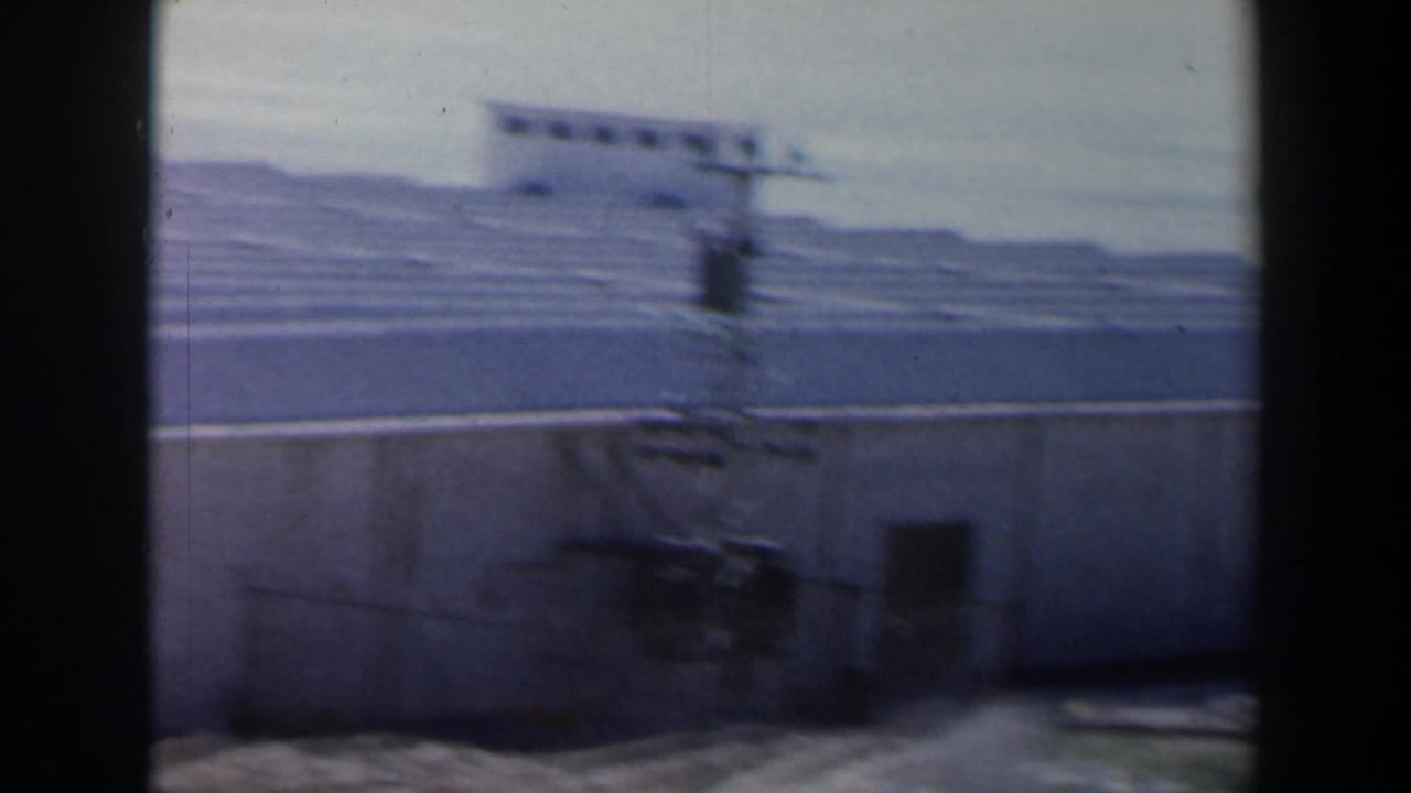 Blurred concrete structure with ribbed roof, low wall, dark frame edges, and distant hills.