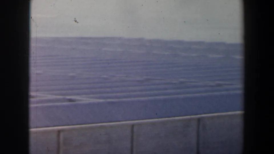 1960 Israel 8mm frame showing a broad ribbed concrete surface beyond a low wall, with distant terrain and film-edge shadows.