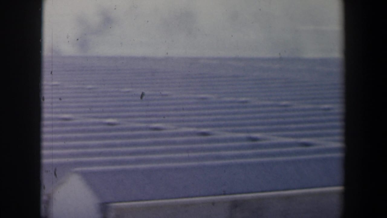 1960 8mm Israel footage shows a corrugated metal roof or wing edge with calm coastal water beyond.