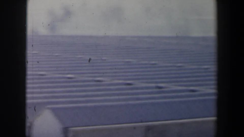 1960 8mm Israel footage shows a corrugated metal roof or wing edge with calm coastal water beyond.