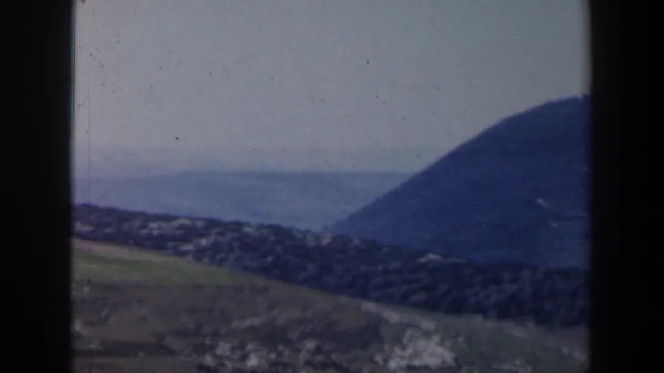 Aerial 8mm view over an Israeli coastal hillside settlement with water and a rounded mountain beyond.