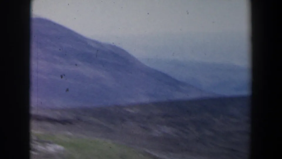 1960 8mm aerial frame shows a rolling Israeli hillside with hazy water or valley distance beyond.