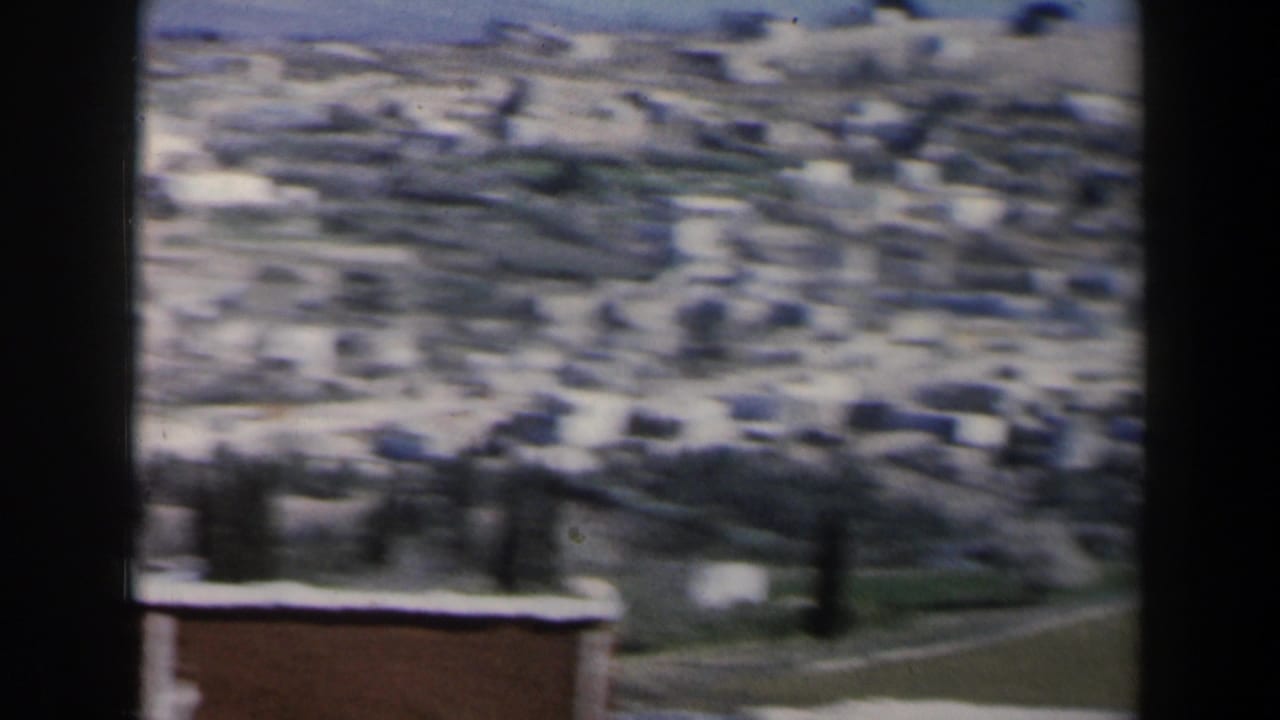 Blurred distant town buildings on a dry hillside with a road and open ground below.