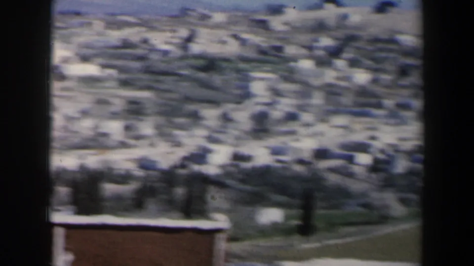 Soft 1960 Israel 8mm view of a hillside town, with pale buildings, dry slopes, a road, and open terrain seen from a distance.
