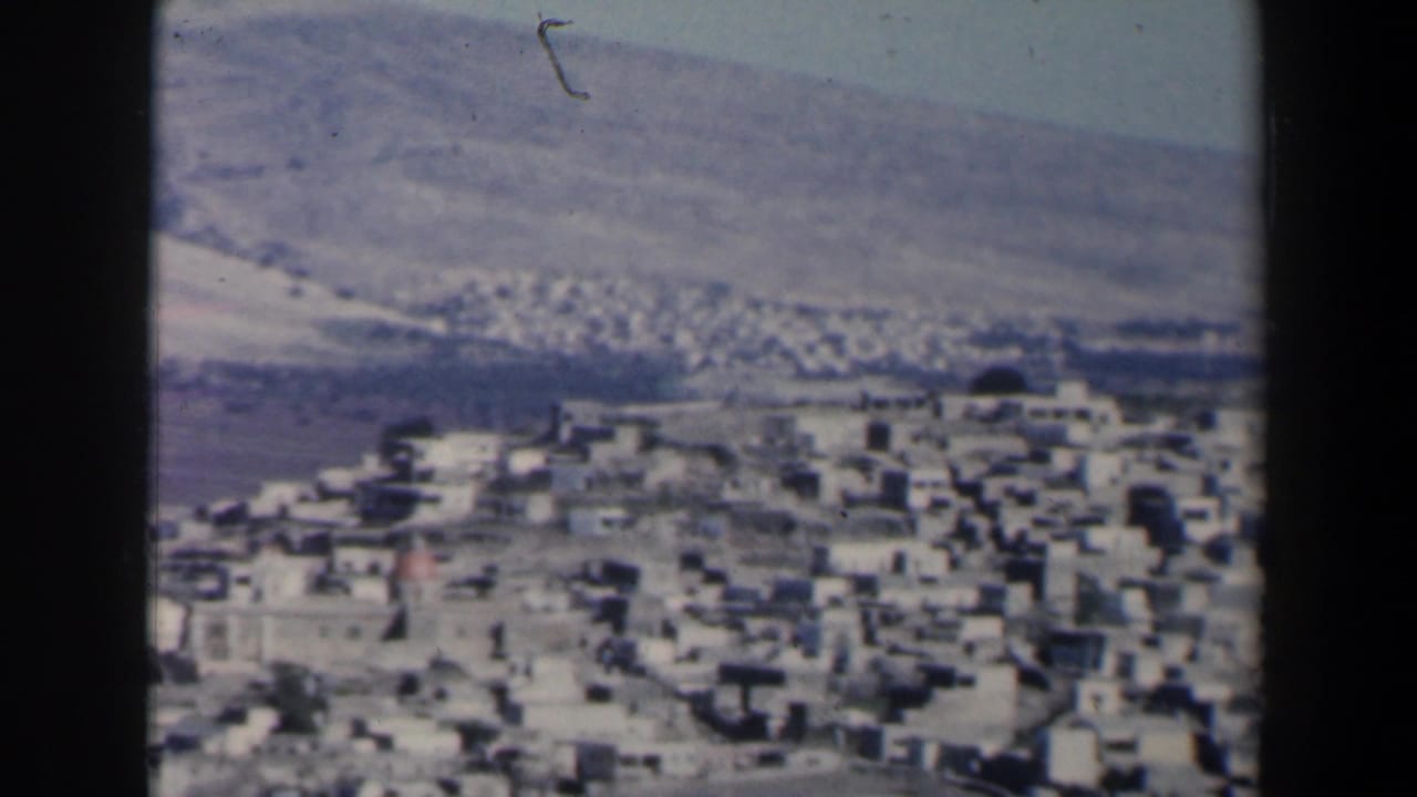 White buildings spread across a hillside beneath a barren rocky slope.