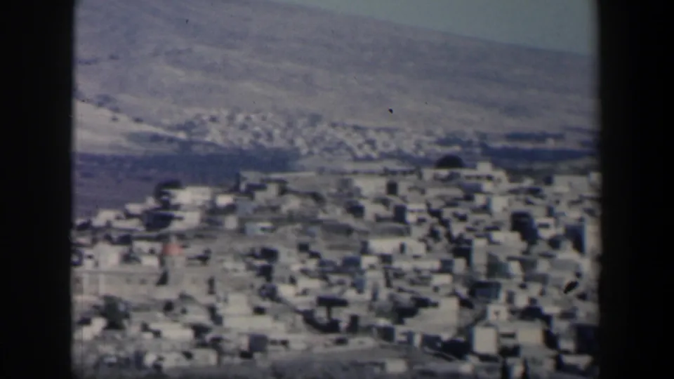 Handheld 1960 Israel 8mm view of a white hillside settlement set against dry mountain slopes and sparse vegetation.