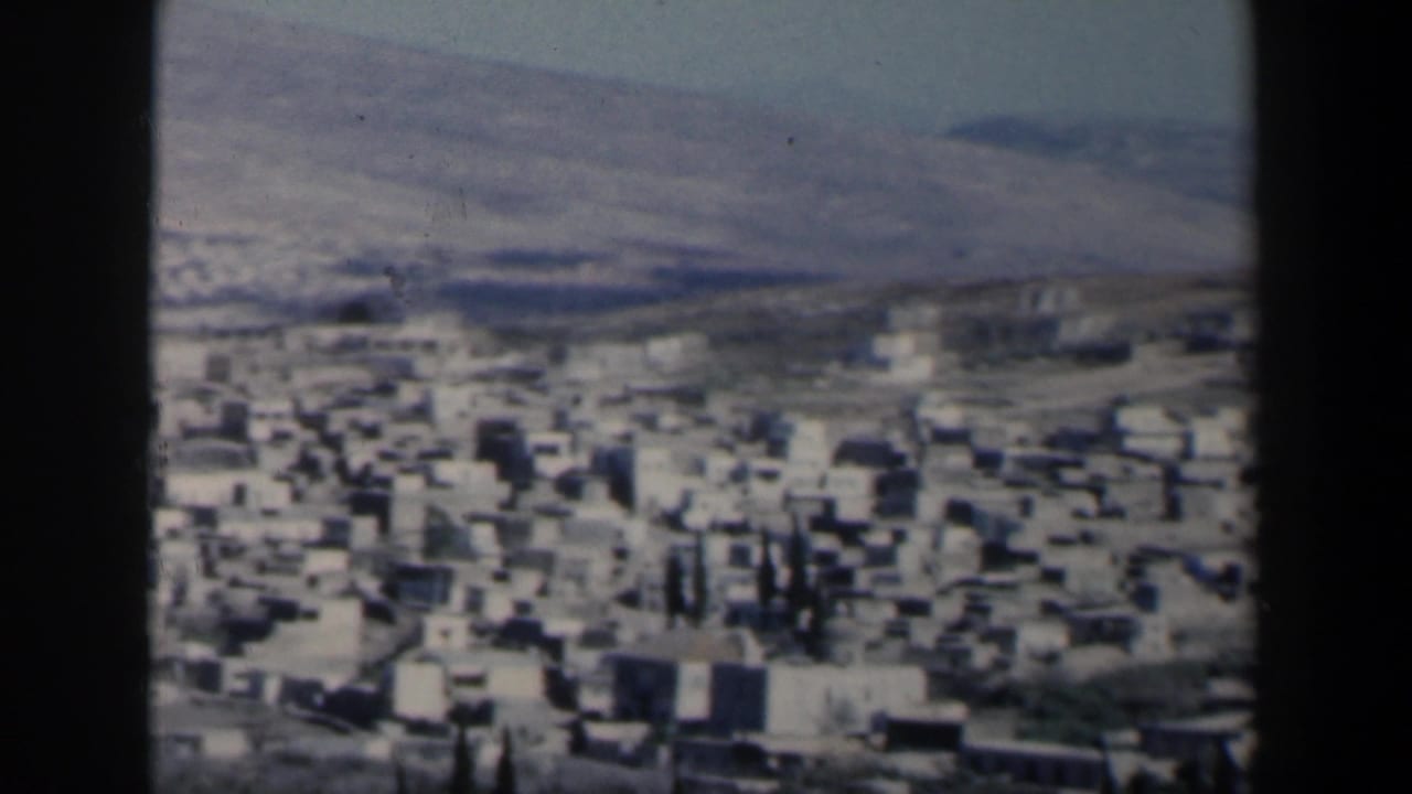 Soft aerial view of white buildings spread across arid hills.